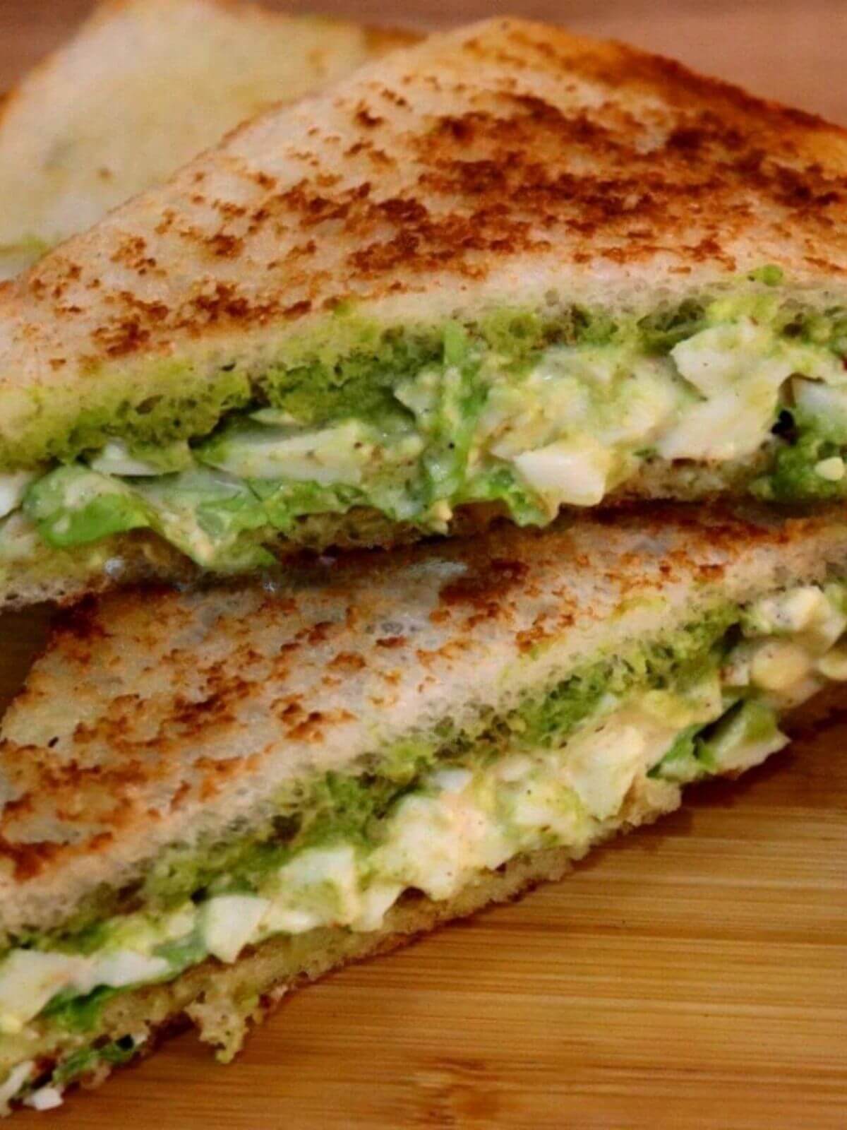 Halved egg mayo sandwich on a wooden chopping board, with the creamy filling clearly visible.
