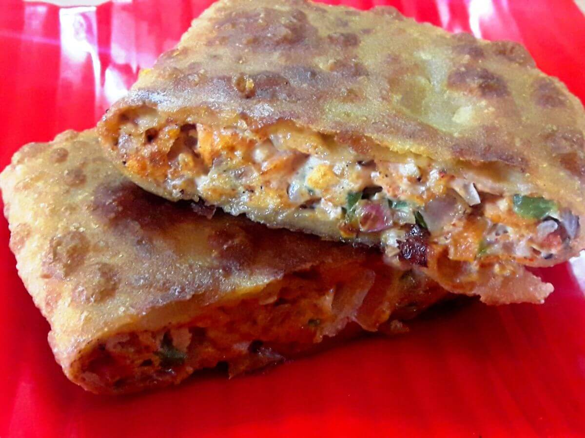 close-up of egg paratha, cut in half and stacked on a red color plate.
