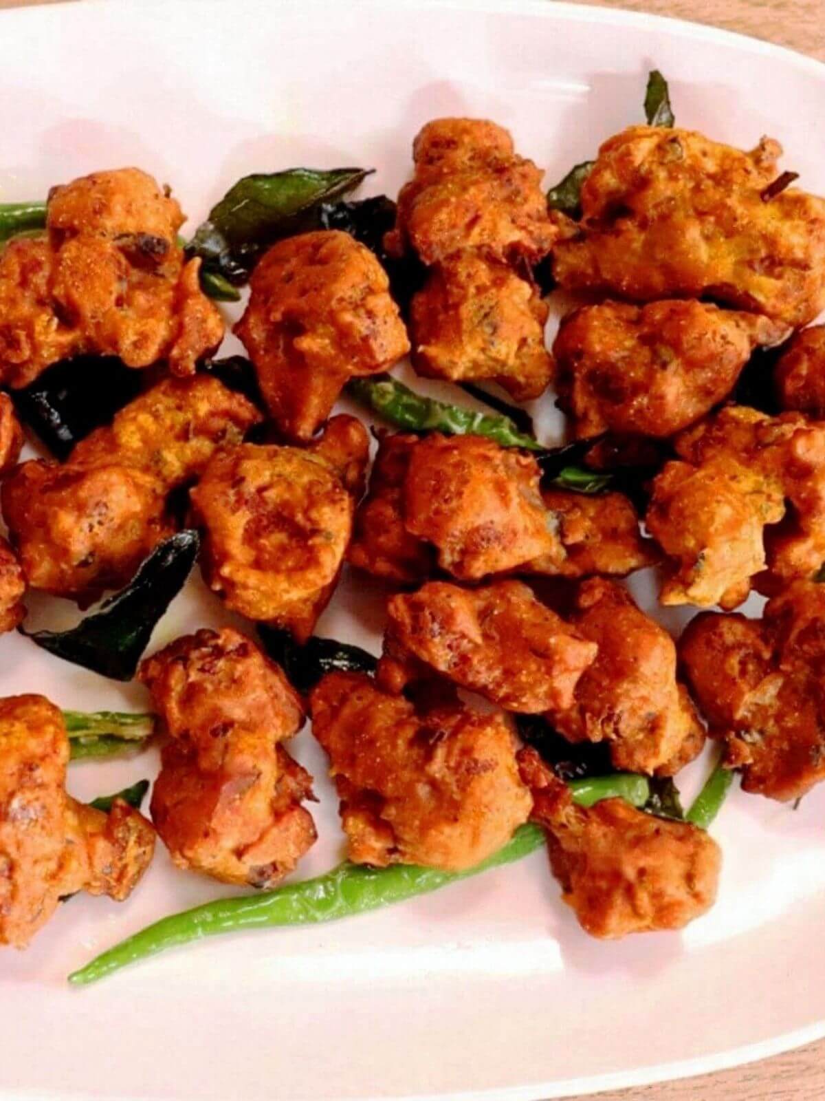 close-up of gobi 65 served on a white plate. Garnished with fried green chilies and curry leaves.