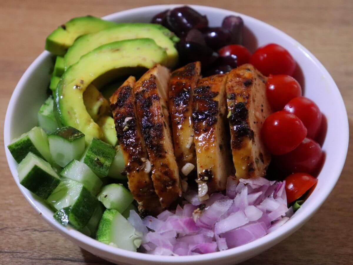 close-up of grilled chicken salad with avocado served in a bowl.