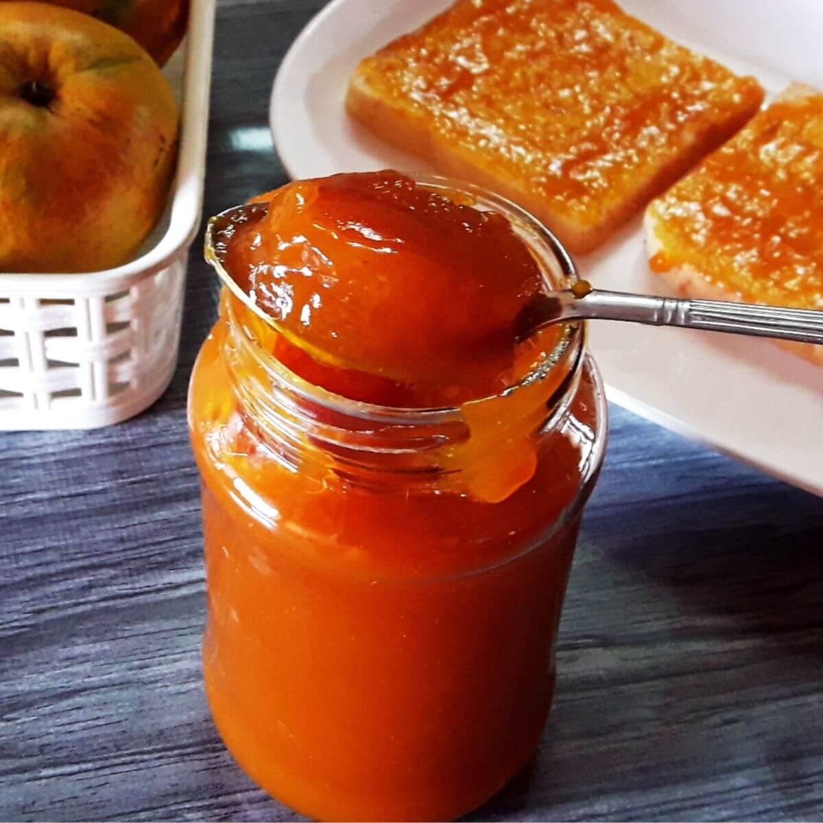 A close-up shot of homemade mango jam in a glass jar, with a spoon full of jam balanced on its rim.