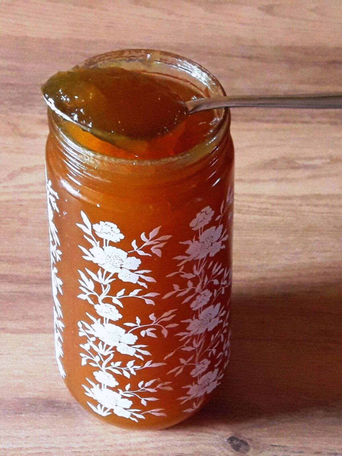 A close-up of homemade pineapple jam in a jar, with a spoonful of jam resting on the rim.