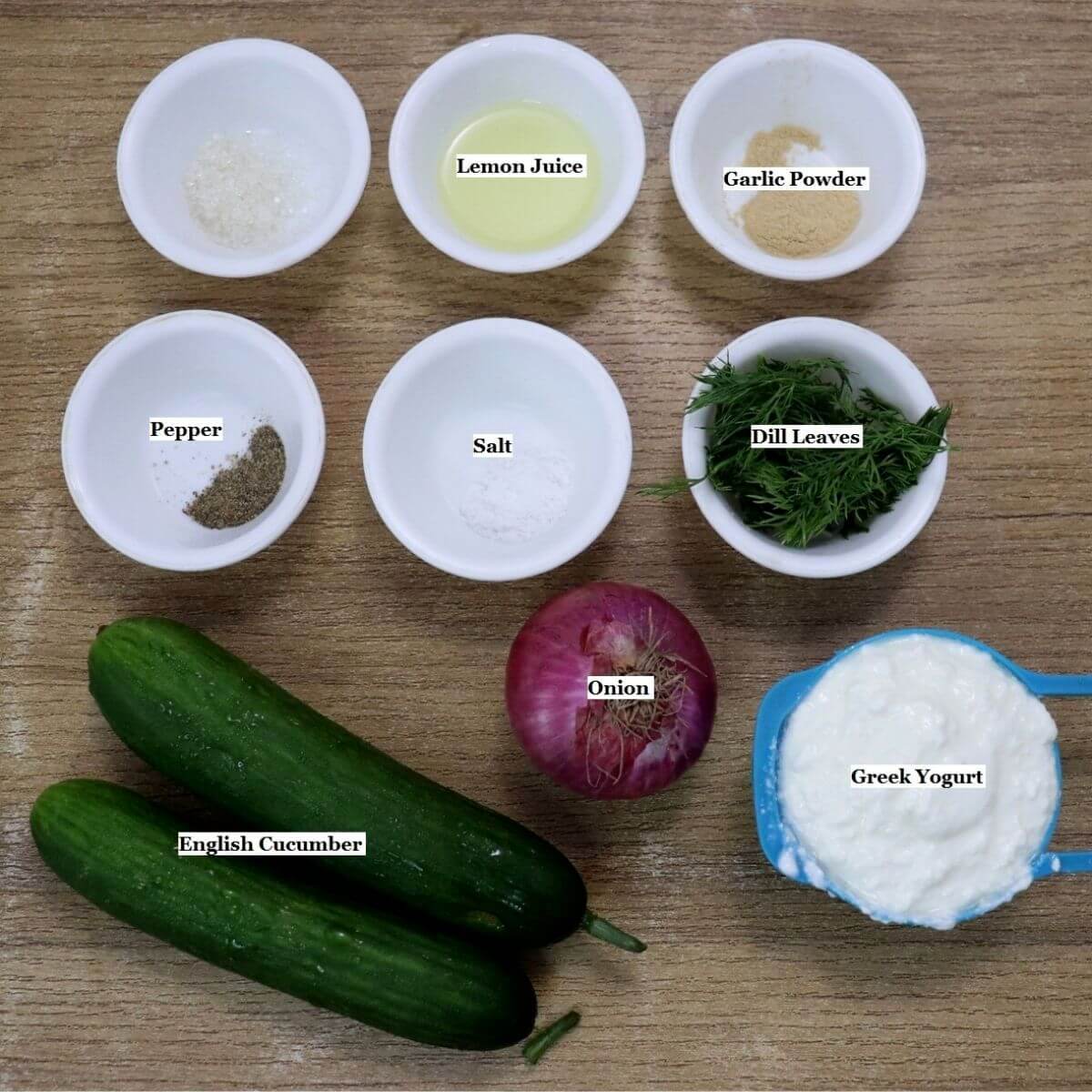 individually labeled ingredients to make greek yogurt cucumber salad are laid out on a table.