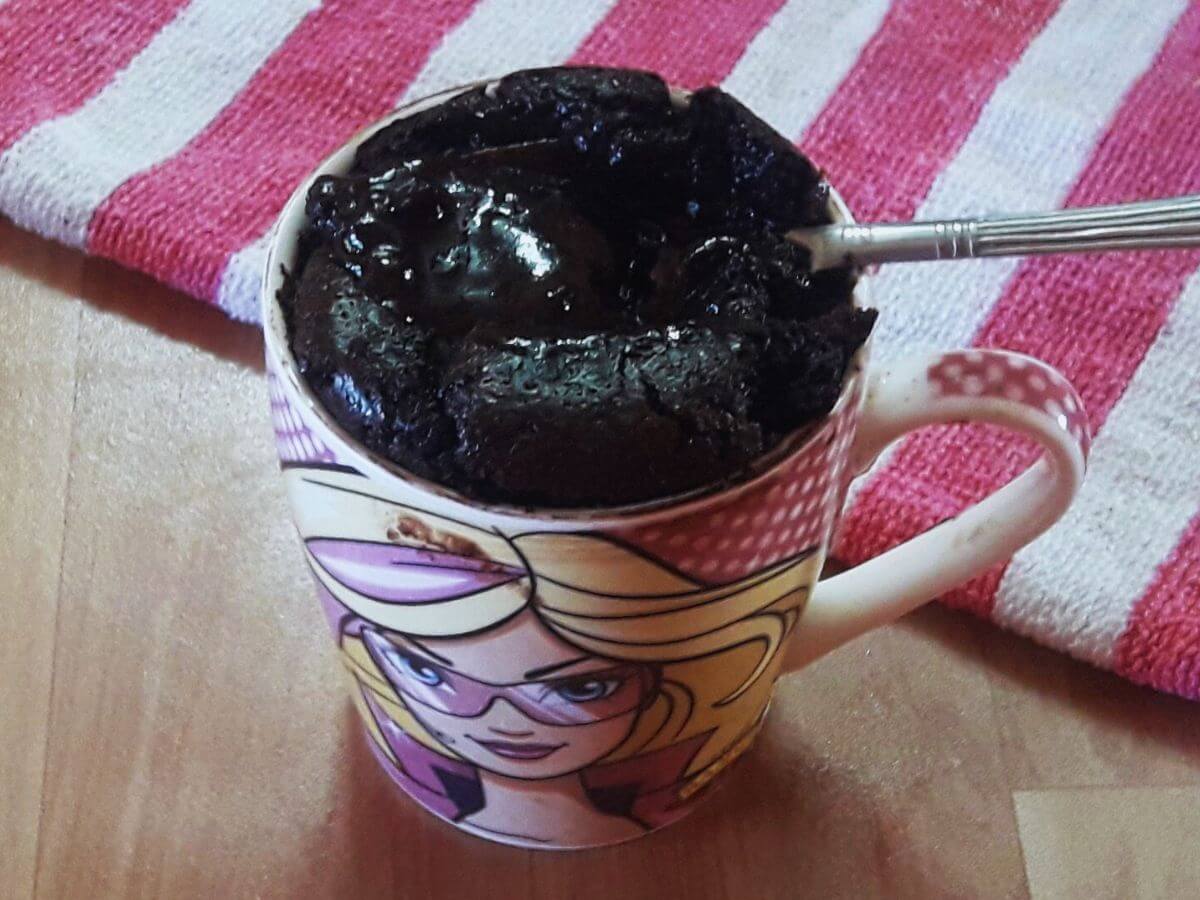 A close-up of a microwave chocolate mug cake, with a spoonful of molten chocolate lava resting on the mug's rim.