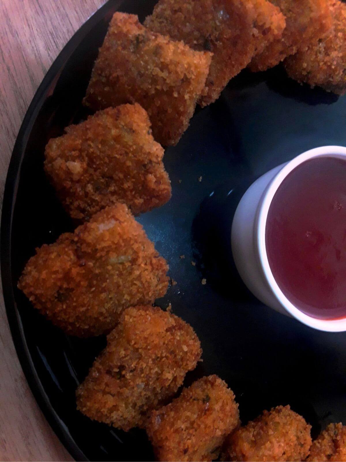 close-up of poha cutlet served in a black plate with ketchup.