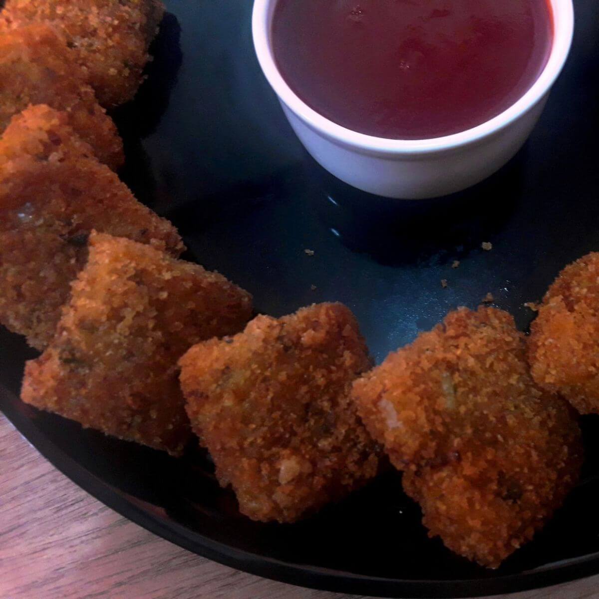 close-up of poha cutlets served in a plate with tomato ktchup.