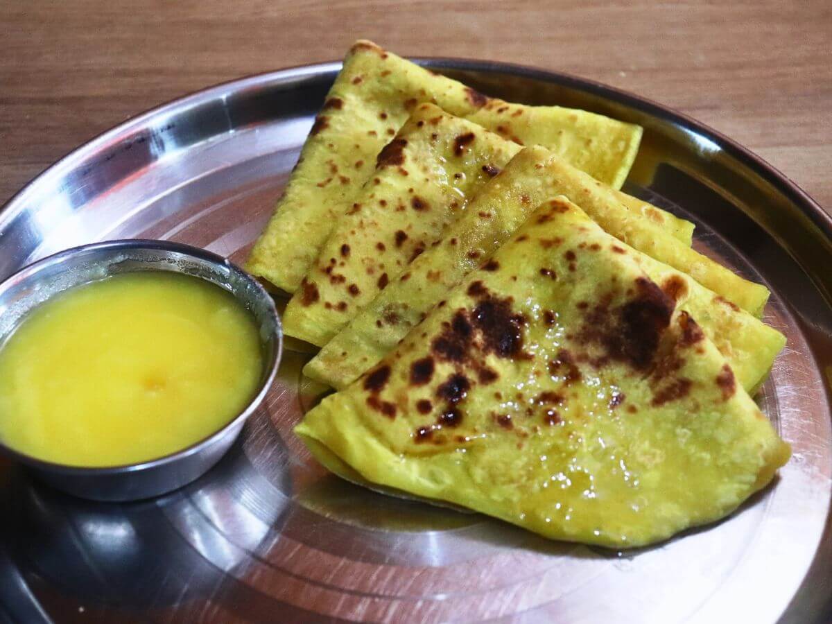 close-up of 4 maharashtrian puran poli served in a plate with a small bowl of ghee on side.
