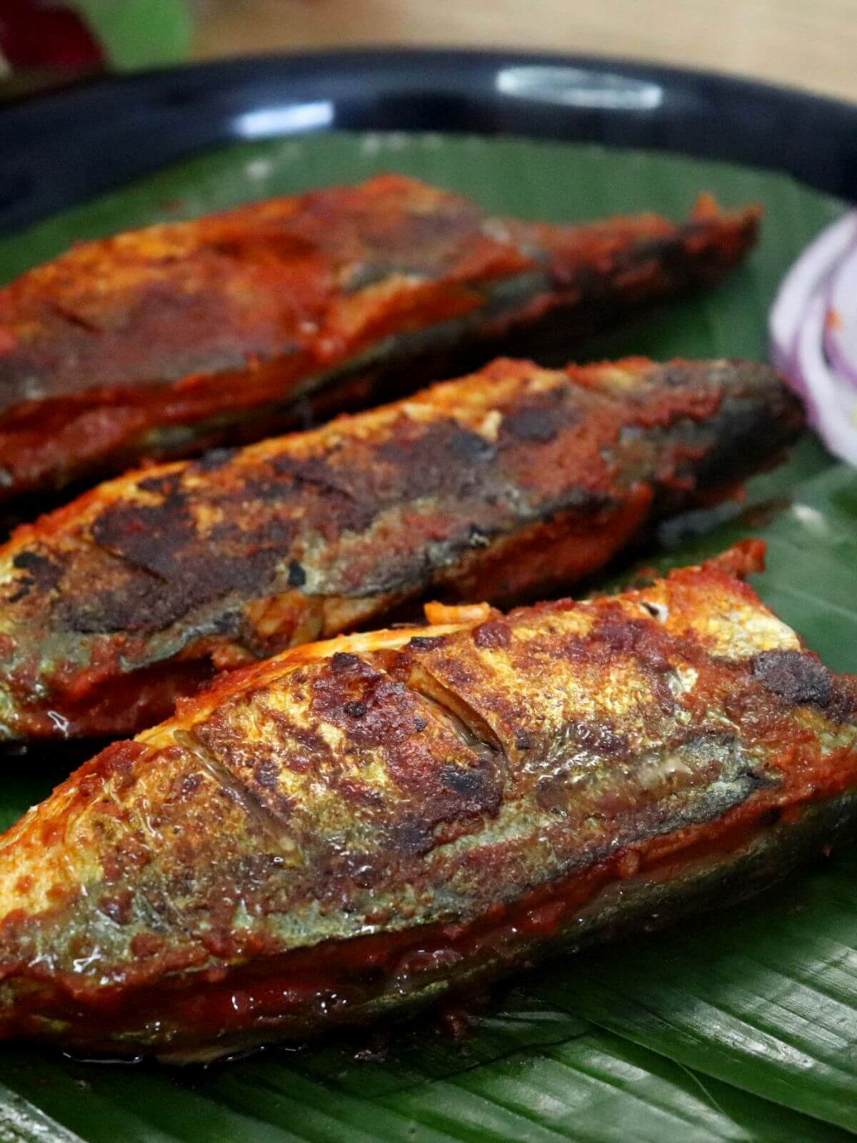 A close-up of recheado fish fry, served on a banana leaf which is placed on a plate.