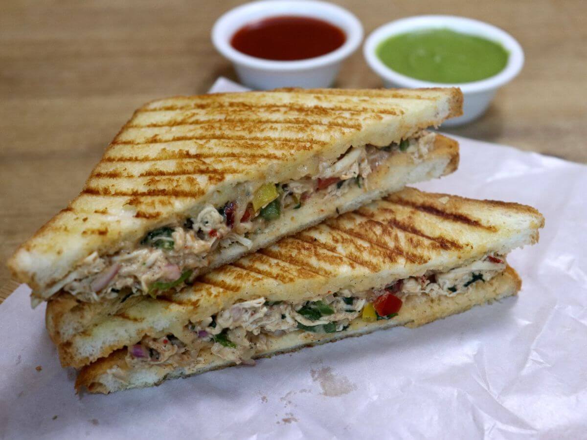 close-up of shredded chicken sandwich served with tomato ketchup and green chutney on the side.