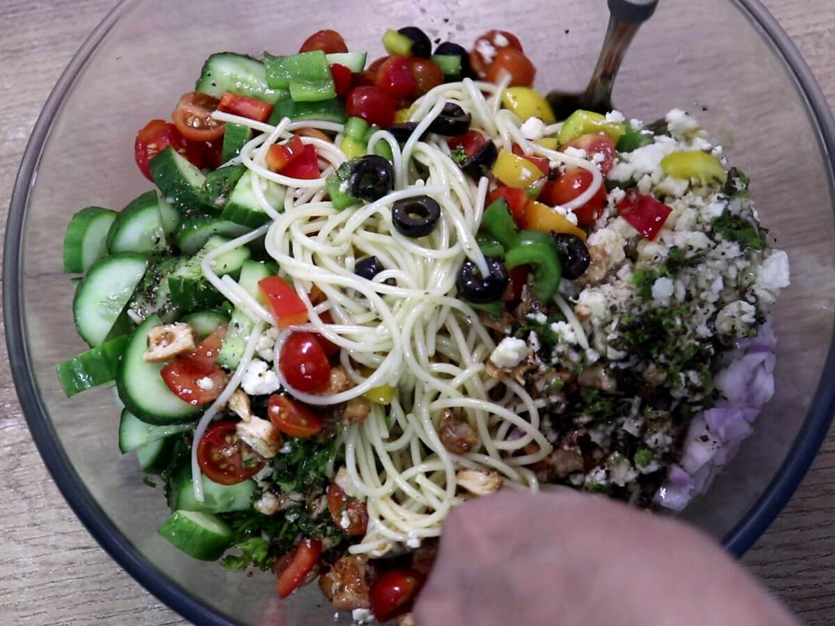 Close-up of a vibrant spaghetti salad being mixed with dressing.
