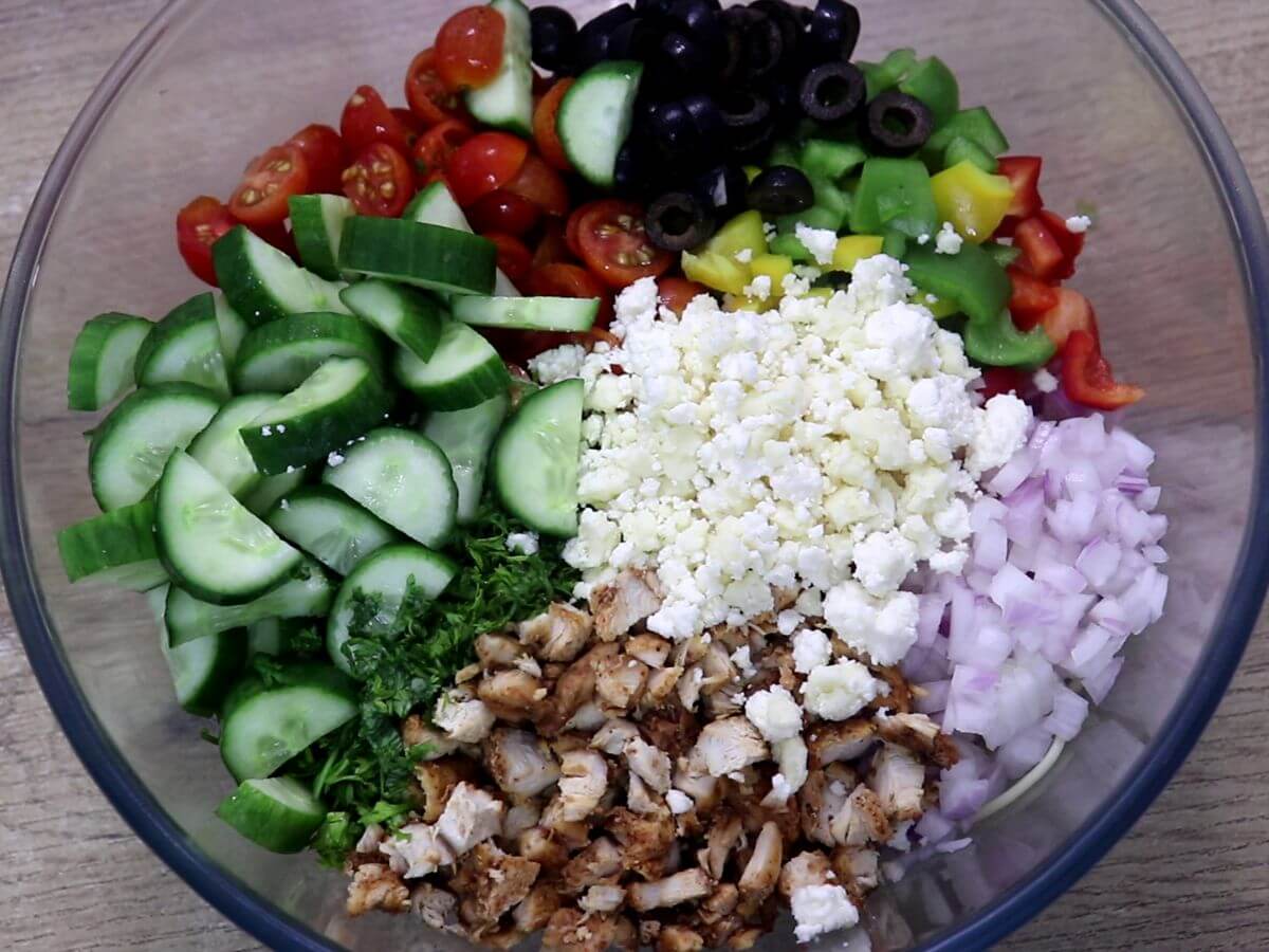 A mixing bowl containing spaghetti salad with colorful vegetables, chicken and feta cheese.