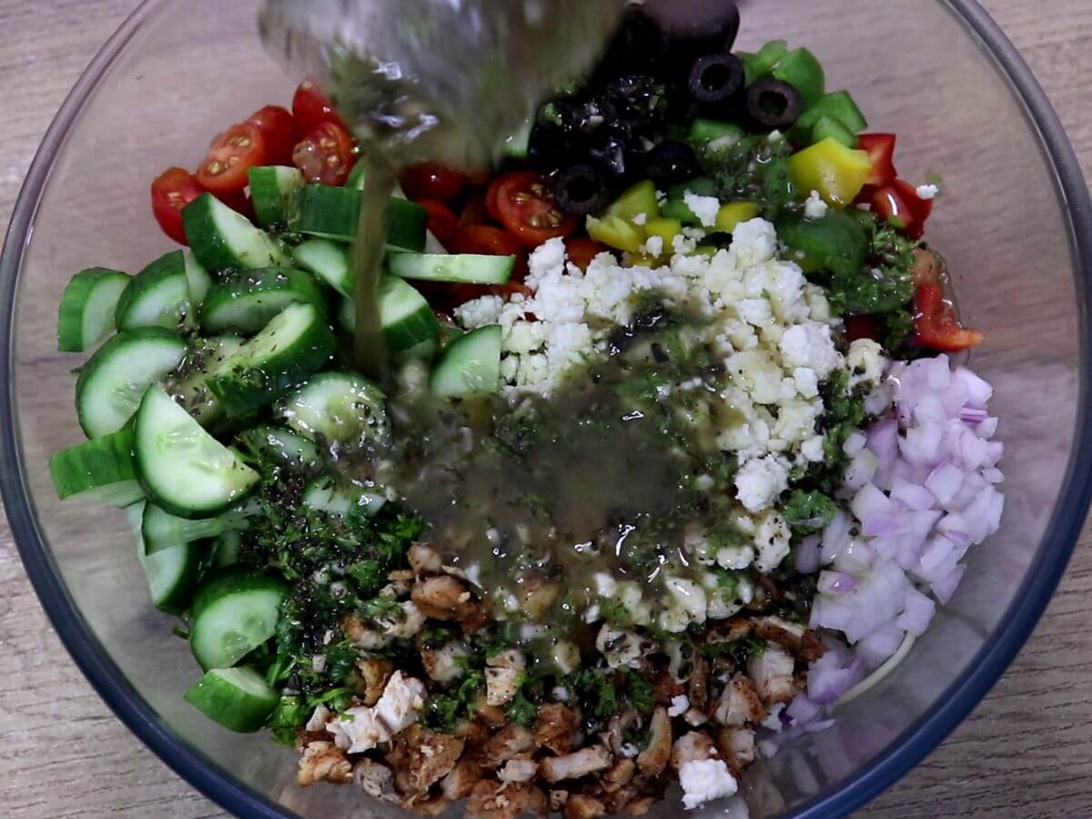 pouring mediterranean salad dressing on chicken spaghetti salad.