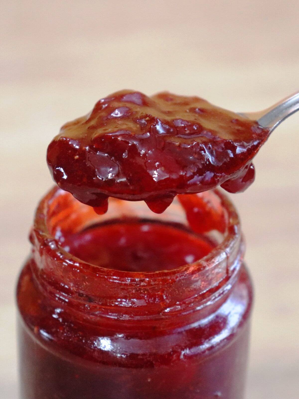 Spoonful of strawberry jam over a jar of strawberry jam.