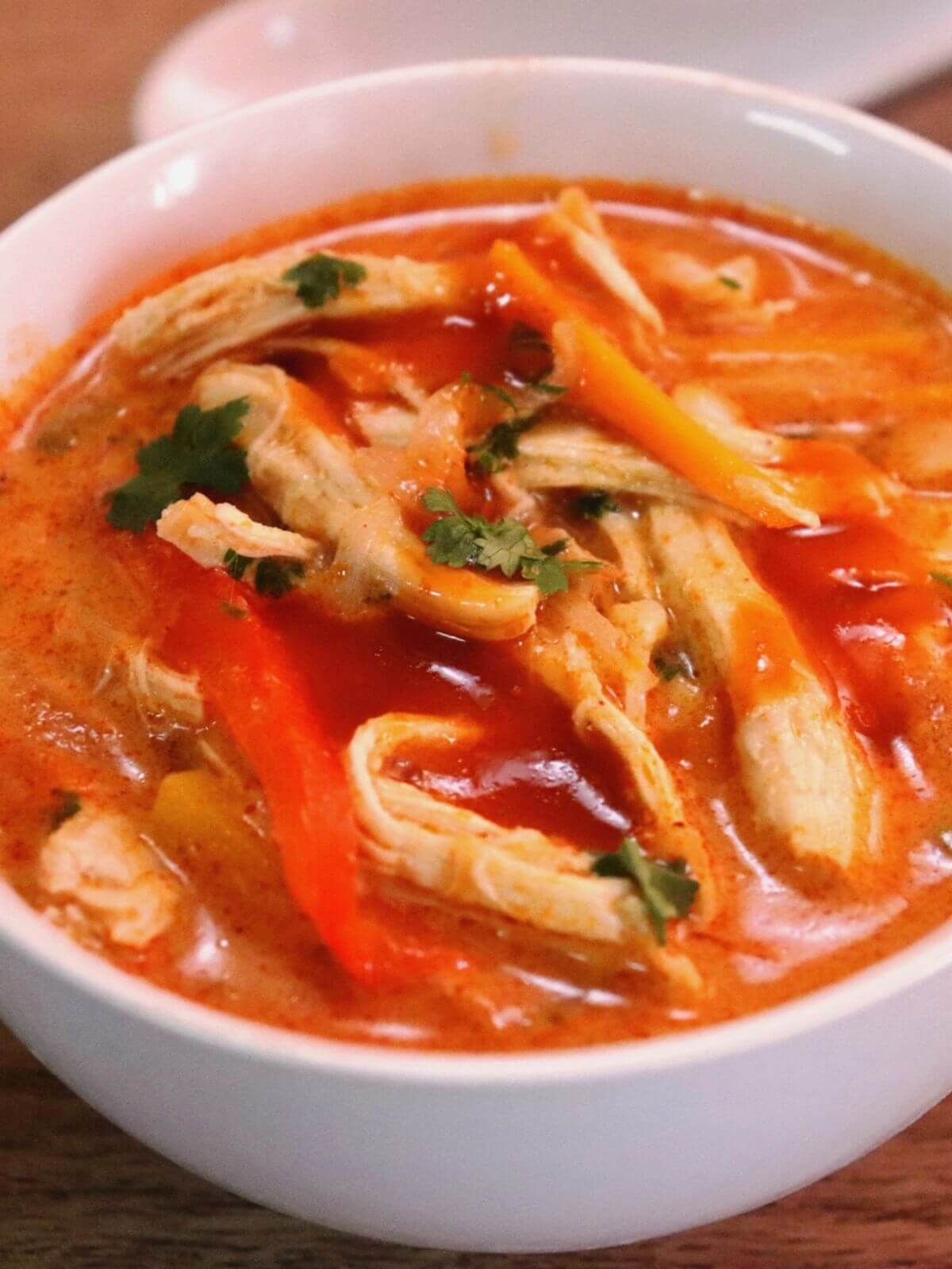 close-up of thai red curry chicken soup served in a white bowl.