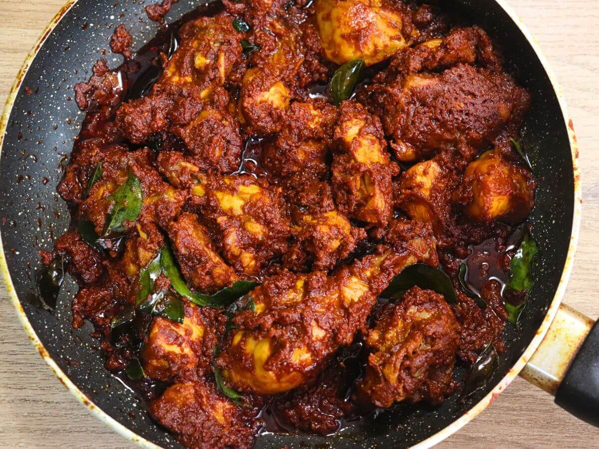 chicken ghee roast in a black pan on a brown countertop.