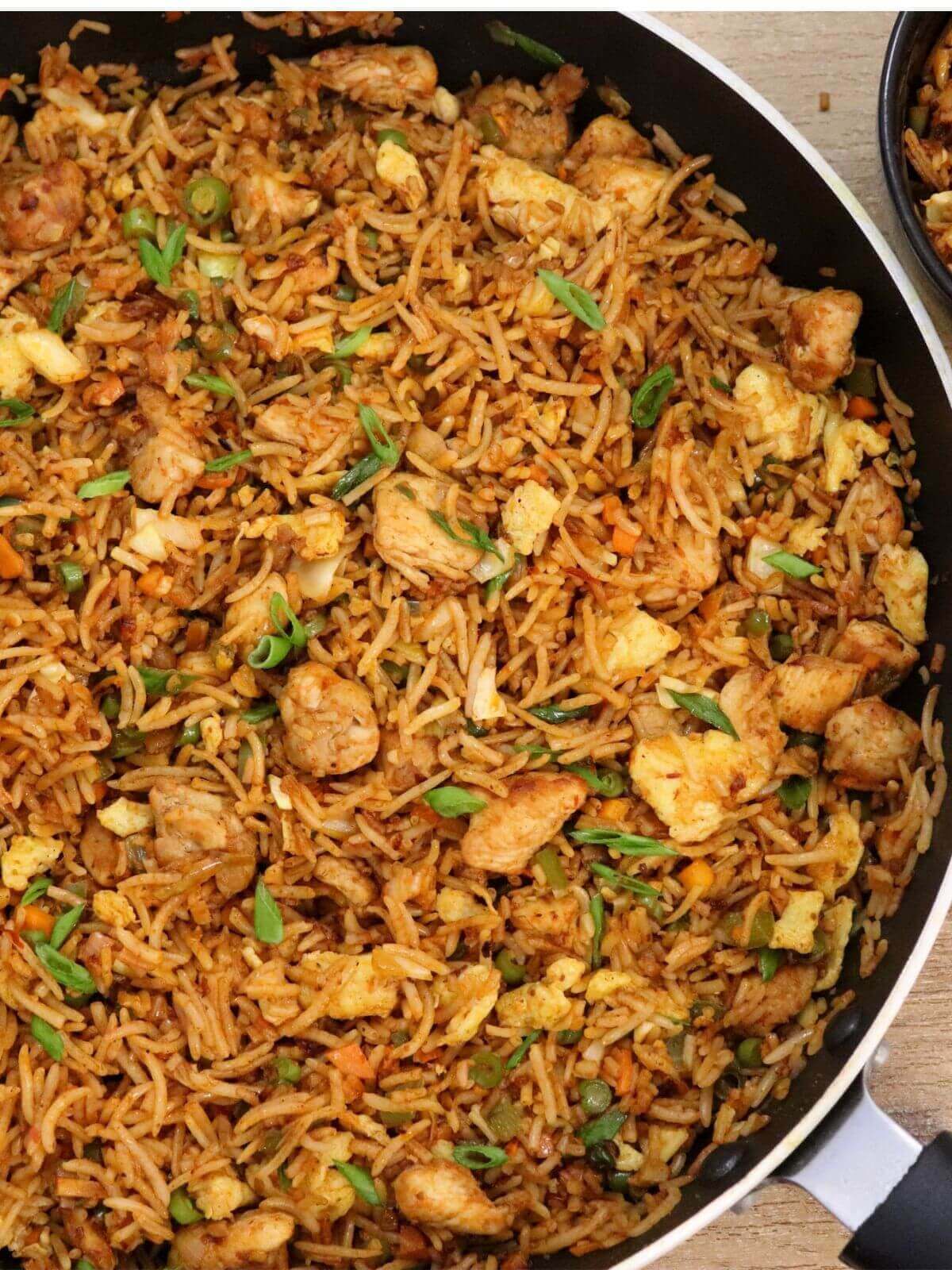 spicy schezwan chicken fried rice in a black colored pan on a brown counter top.