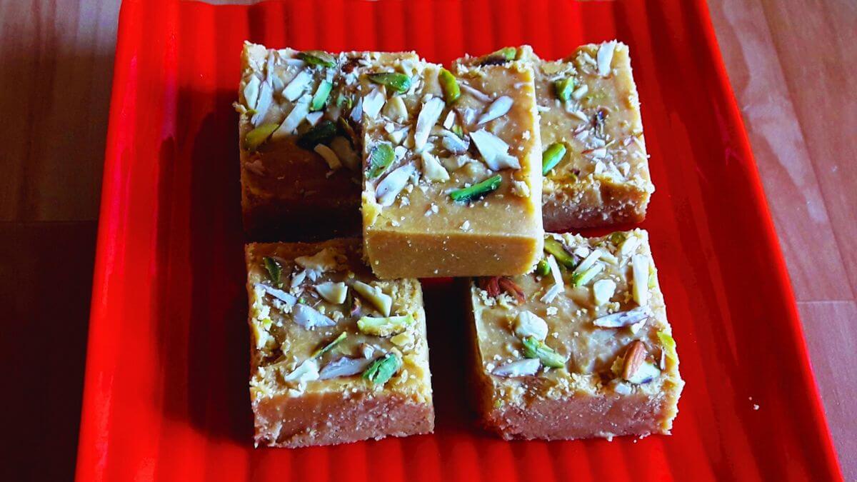 besan burfi placed on a red colored palte on a brown counter top.