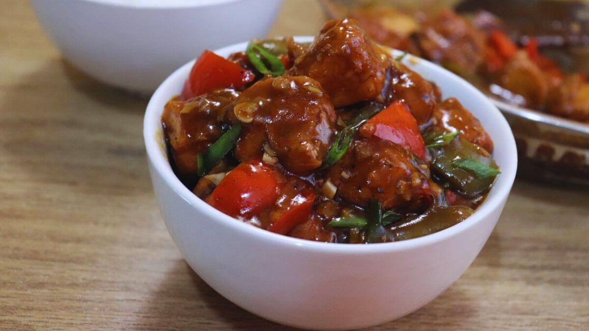 indo chinese chilli chicken gravy served in a white bowl. A pan filled with remaining chilli chicken gravy is placed on the side.