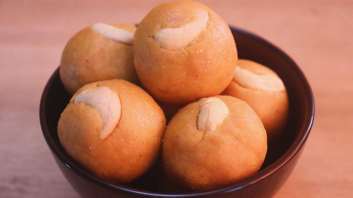 moong dal ladoo with jaggery stacked on a black color bowl on a brown counter top.