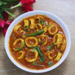 goan style squid masala served in a white bowl on a brown counter top.