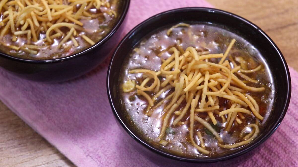 A bowl of chicken manchow soup topped with crispy fried noodles and garnished with spring onions.