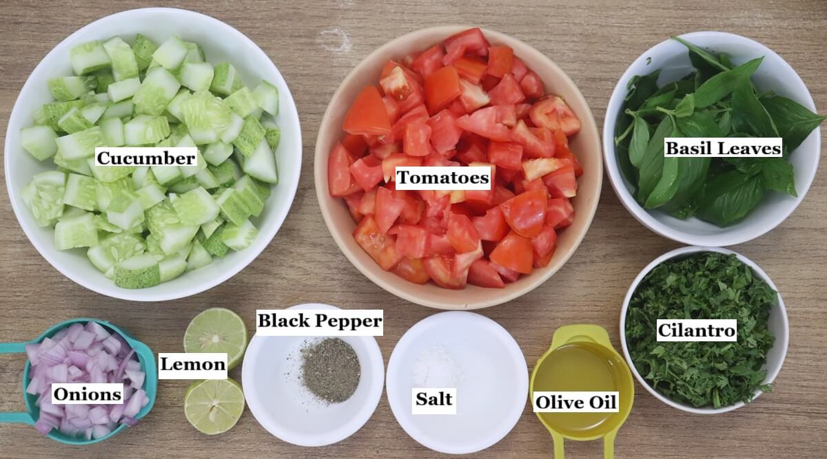 indivially labelled ingredients to make mediterranean cucumber tomato salad recipe are laid out on a table.