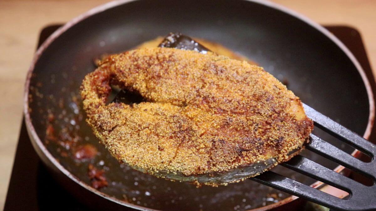 crispy rava fried fish held on a spatula over the pan.