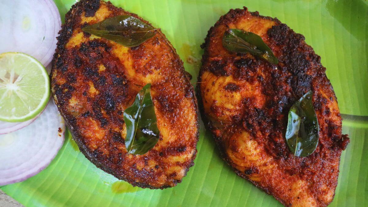andhra fish fry (chepa vepudu) served on a green plate with sliced onions and a lemon slice.