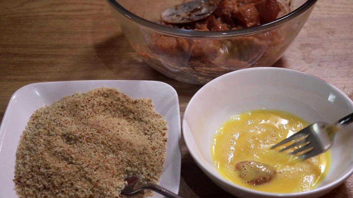 Chicken pieces being dipped in egg mixture for making crispy chicken nuggets.