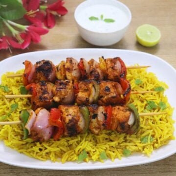 Harissa chicken skewers arranged on a plate of fluffy yellow rice.