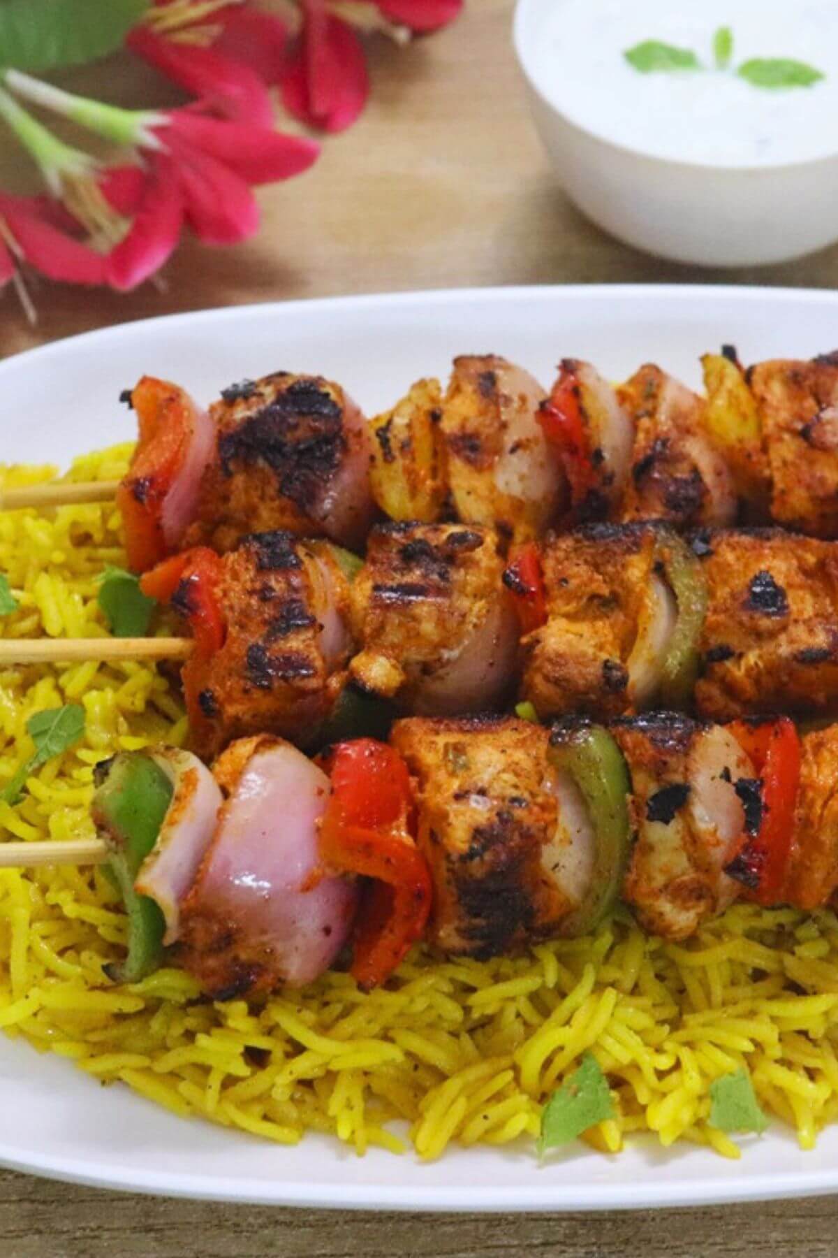 harisssa chicken skewers served over a plate of yellow rice.