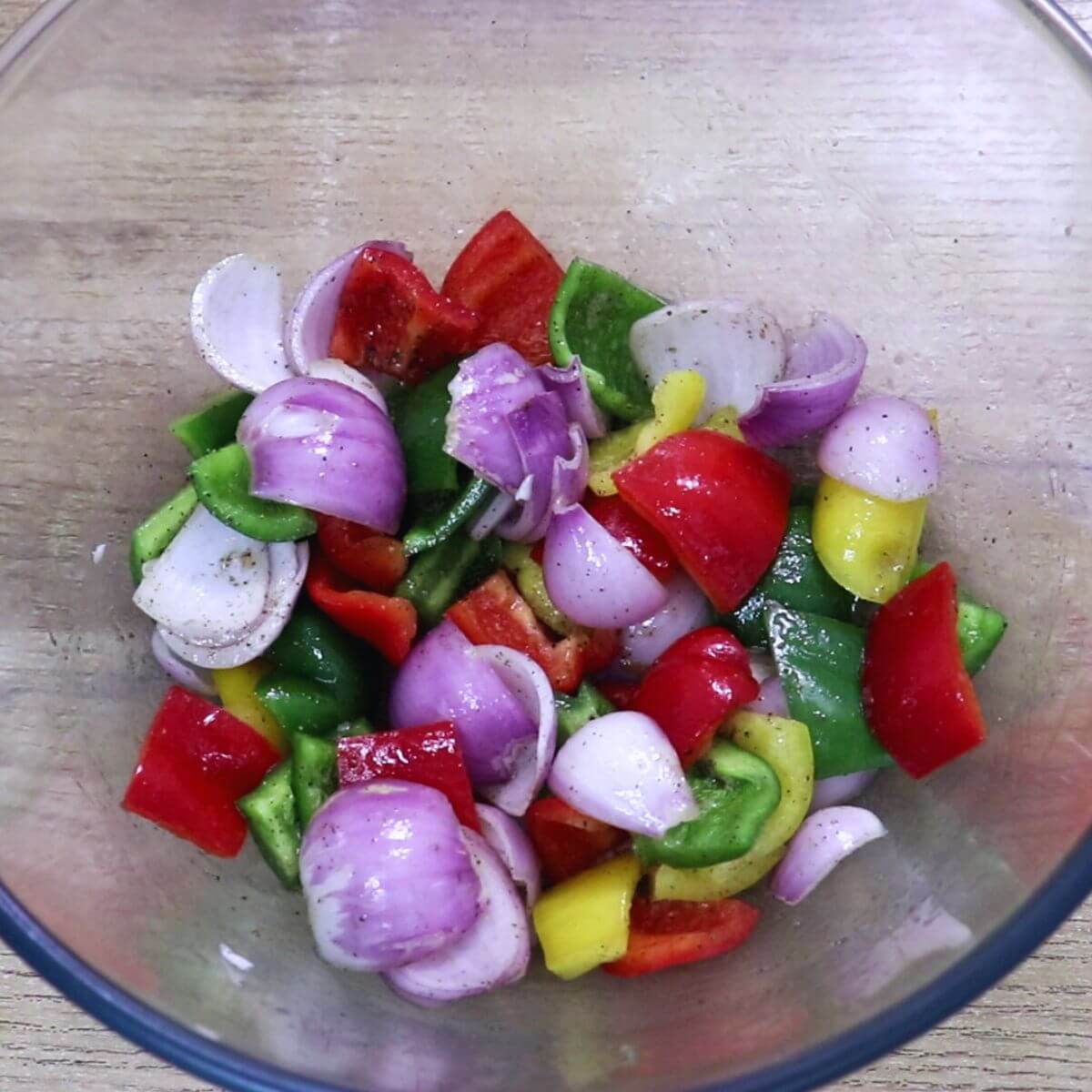 Tossing onions and bell peppers with salt, pepper, and lemon juice for harissa chicken skewers.