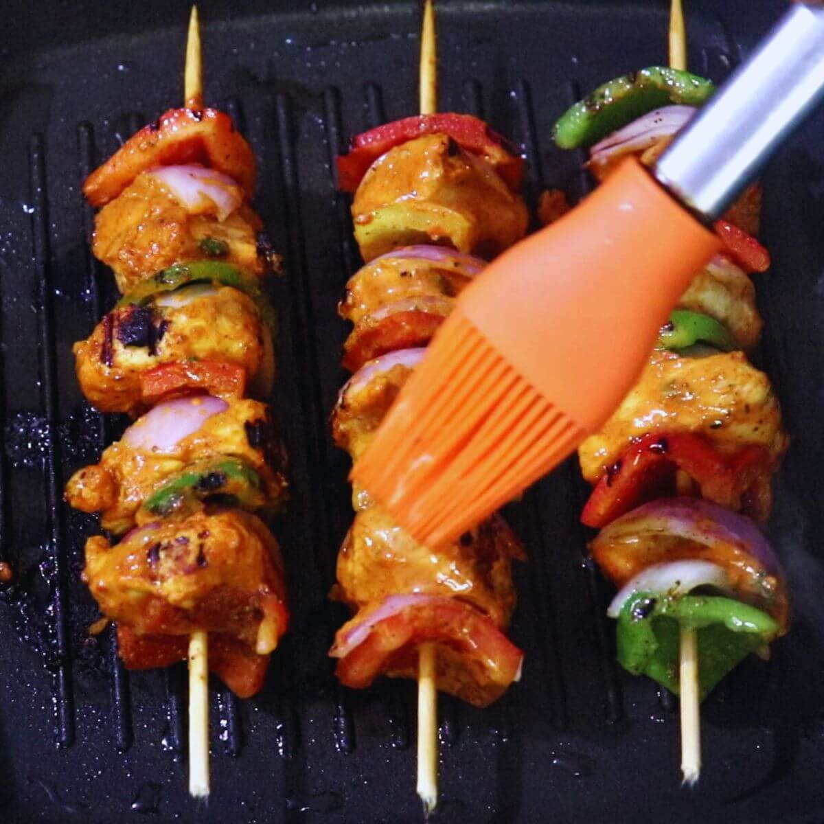 Basting oil on grilled harissa chicken skewers for juicy, flavorful results.