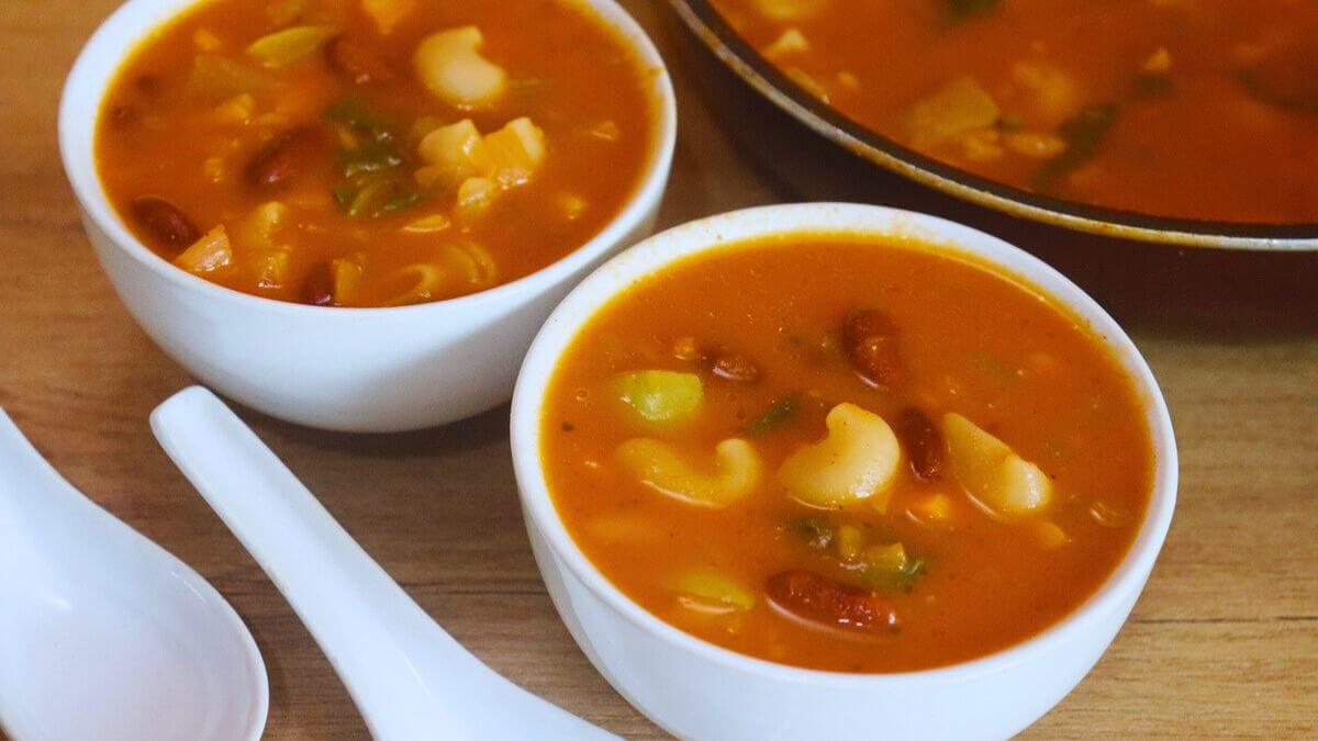 minestrone soup served in two white bowls are placed on a brown countertop.