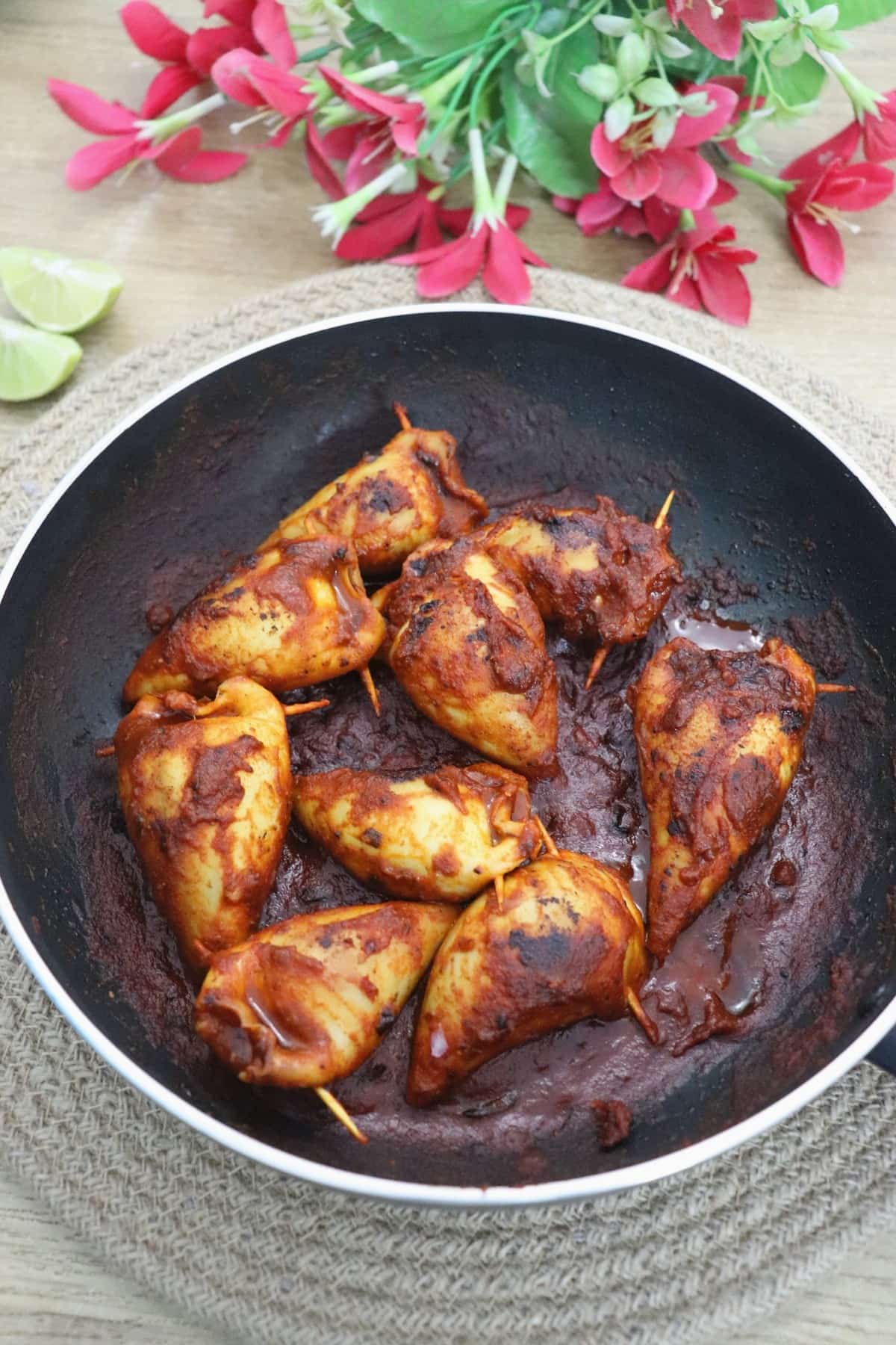 stuffed squids in a pan with lemon wedges on the side.