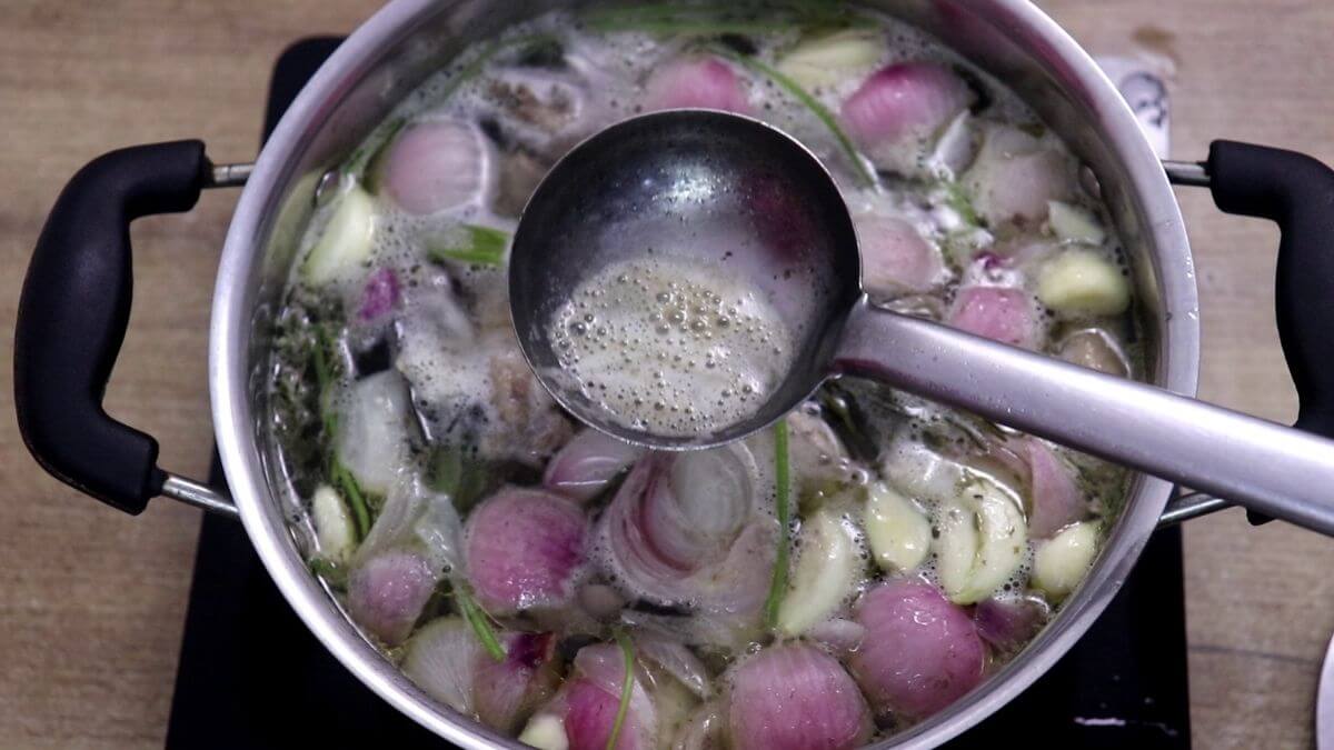 Foam being skimmed from simmering chicken stock.