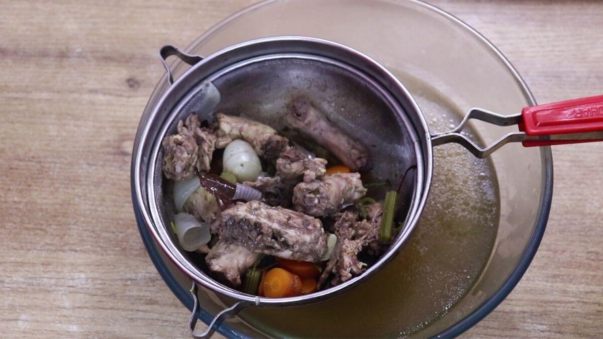 Homemade chicken stock being strained through a fine mesh sieve.
