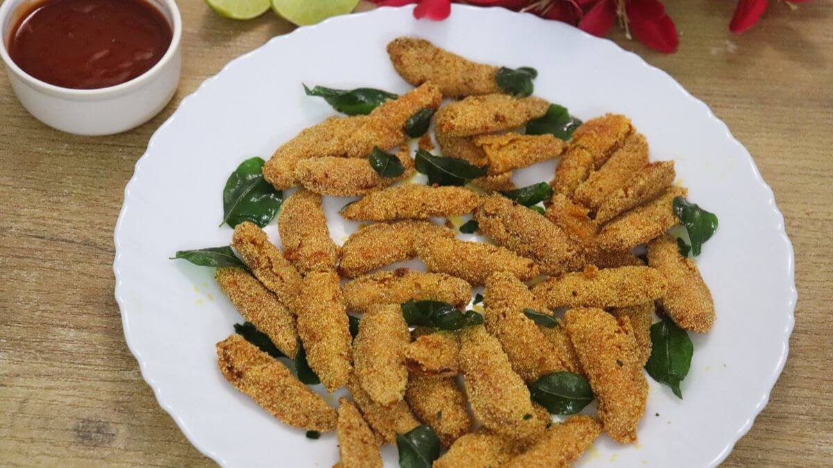 silver fish fry served on white plate with ketchup and lemon wedges on the side.