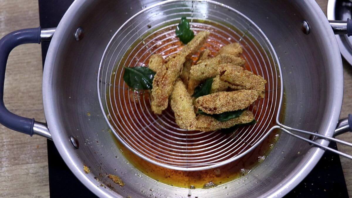 Fried silver fish lifted from hot oil using a wire ladle