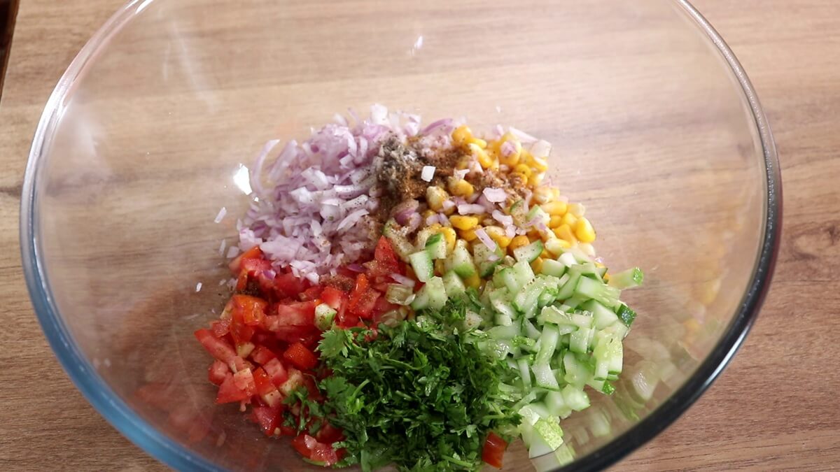 Fresh corn salsa in a bowl with tomatoes, onion, cucumber, and coriander.