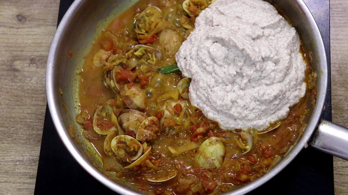 Adding ground coconut paste to clam curry.