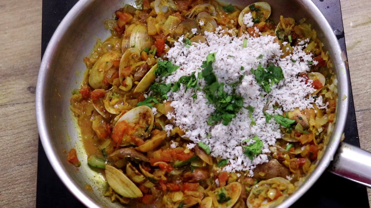 Adding grated coconut to the cooked clams.