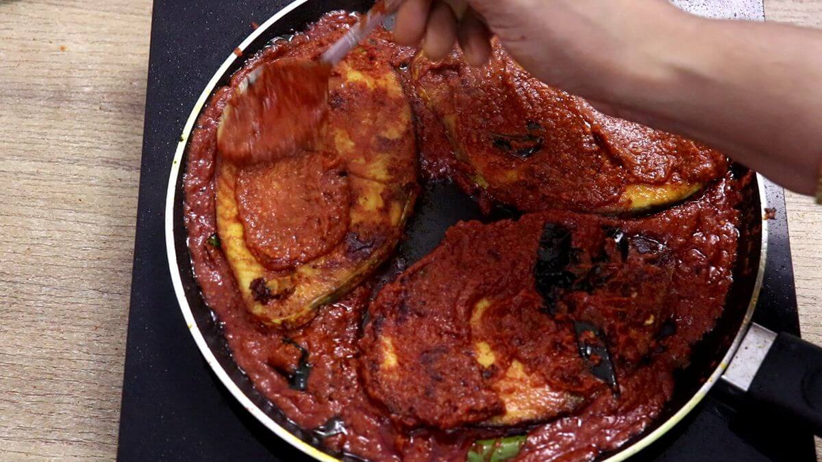 applying masala with a spoon on the fish for tawa fry recipe.