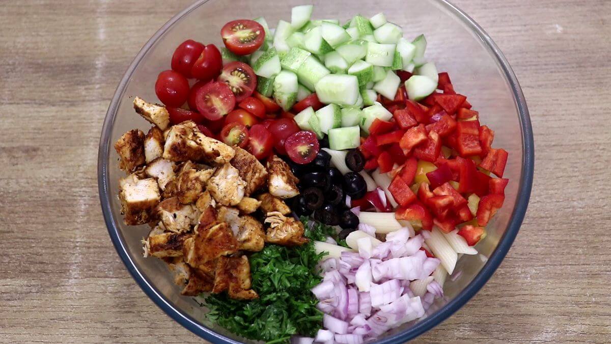 assembling vegetables and cooked chicken for pasta salad in a bowl.