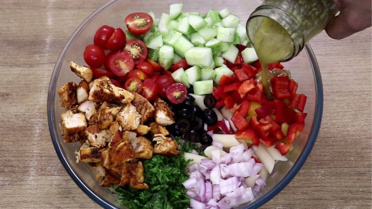 pouring the dressing over lemon chicken pasta salad with feta.