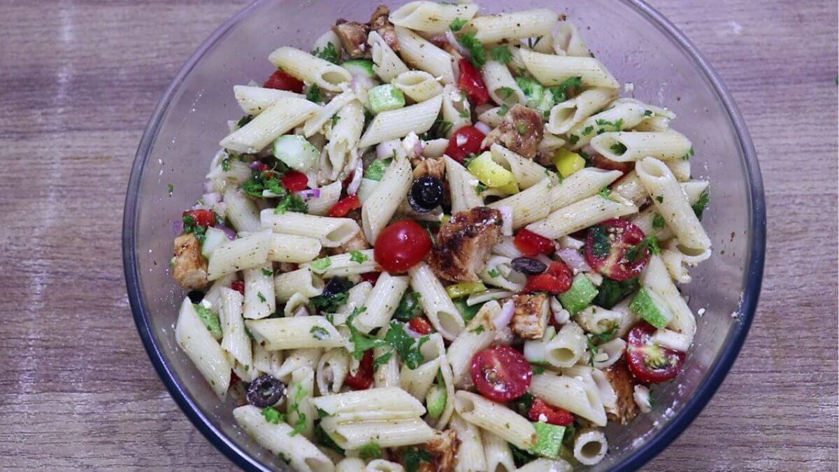 tossing lemon chicken pasta salad with feta.