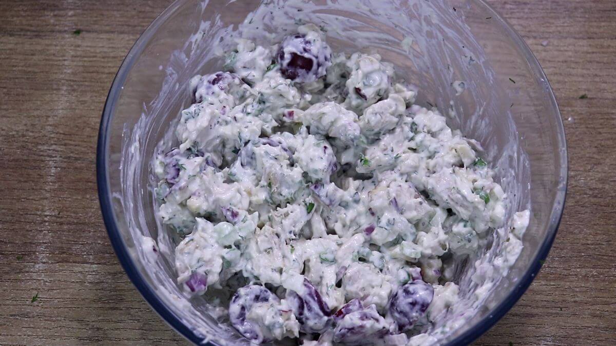 Mediterranean Greek Yogurt Chicken Salad being tossed until evenly coated.