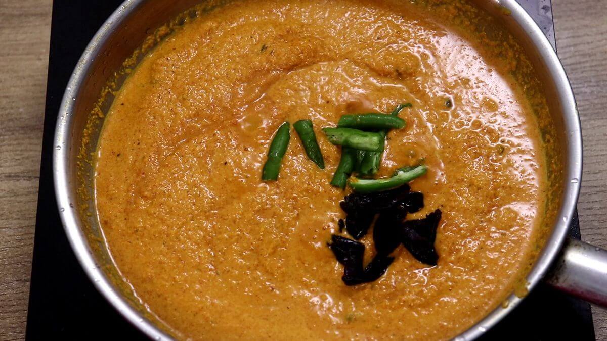 Coconut masala cooking with kokum and green chilies in a pan.