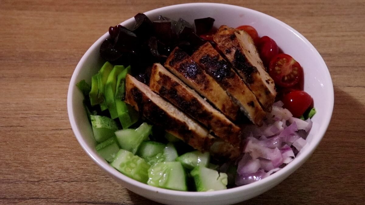 assembling the grilled chicken avocado salad in a bowl.