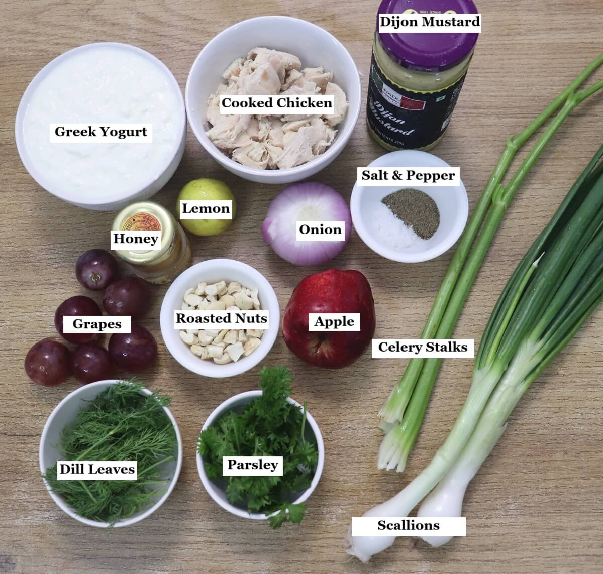 individually labelled ingredients to make mediterranean greek yogurt chicken salad are laid out on a table.